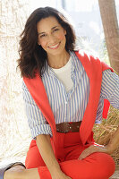 An older brunette woman wearing a blue-and-white striped shirt with a salmon-coloured jumper and trousers