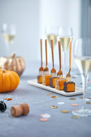 Pumpkins aper cubes on golden forks with poppy seeds and champagne glasses