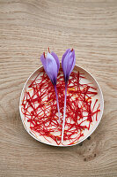 Safranfäden (Crocus sativus) und Safranblüten in weißer Schale