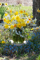 Easter bouquet of daffodils and bridal spears in the flower bed with forget-me-nots, basket with Easter eggs in the background