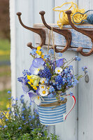 Spring bouquet of forget-me-nots, grape hyacinths, daisies, cowslips, and horned violets in cups hung on coat hooks