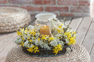 A canning jar as a lantern in a wreath of Forsythia and sloes