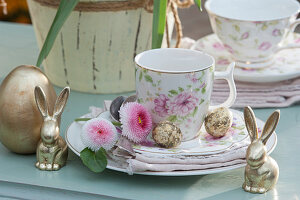 Osterdeko mit goldenen Osterhasen und Osterei, Kaffeetasse mit Ostereiern und Blüten von Tausendschön