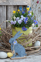 Topf mit Hornveilchen, Strahlenanemone, Traubenhyazinthen und Narzissen in Kranz aus Clematisranken, Ostereier und Osterhase als Osterdeko