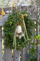 Osterkranz aus Buchsbaum, dekoriert mit Ostereiern und Schleifenband am Gartenzaun