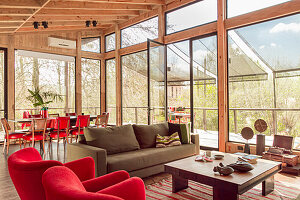 Upholstered furniture in red and taupe and a coffee table in weekend house with glass walls
