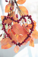 Hagebuttenherz auf künstlichem Zweig mit Herbstlaub