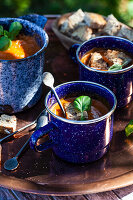 Antique enamel mugs with tomato soup topped with basil and whole wheat croutons