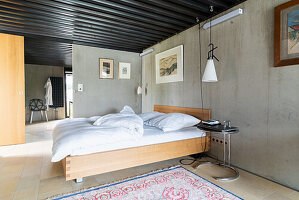 King size bed in the bedroom with concrete walls, ensuite bathroom in the background