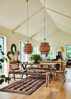 Dining area with wooden table and bench below pendant lights in open-plan interior with oak floorboards