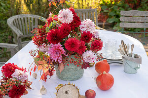 Dahlienstrauß mit Hagebutten und Herbstlaub als Tischdekoration, Kürbisse, Apfel und Geschirr