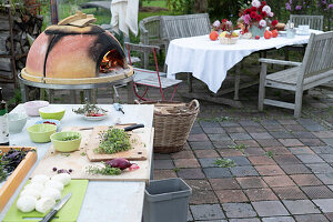 Vorbereitung zur Pizza-Party auf der Terrasse, Pizzaofen mit Holz vorheizen, Arbeitstisch mit Zutaten