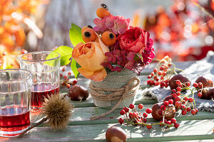Kleines Herbstgesteck aus Rosen, Hagebutten und Hortensienblüten, Vase mit Stoffband umwickelt