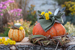 Hollowed out pumpkins as cutlery holders in a grass wreath and as candle holders, chrysanthemum blossoms as decoration