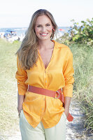 Long haired woman in orange blouse with belt sitting on the beach
