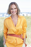 Langhaarige Frau in orangefarbener Bluse mit Gürtel am Strand
