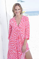 Langhaarige Frau in pink gemustertem Kleid am Strand