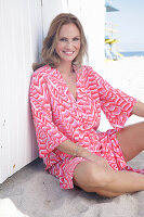Langhaarige Frau in pink gemustertem Kleid am Strand sitzend