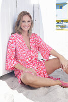 Langhaarige Frau in pink gemustertem Kleid am Strand sitzend