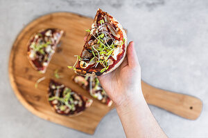 Hand hält ein Stück vegetarische Pizza mit Pilzen und Sprossen