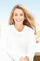 A young woman on a beach wearing a long-sleeved white top and shorts