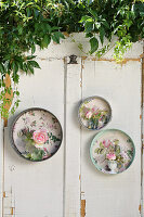 Small vases holding rose 'Eden Rose' in old springform tins backed with floral wallpaper