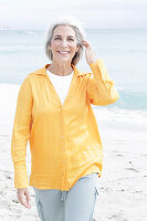 Reife Frau mit grauen Haaren in orangefarbener Bluse und Hose am Strand