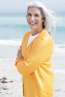 A mature woman with grey hair wearing an orange blouse on a beach