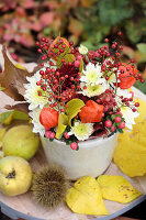 Autumn arrangement with lantern flowers, chrysanthemums, rose hips and hypericum, next to quinces