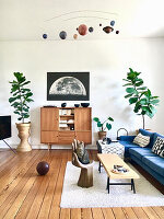 Blaues Polstersofa, Couchtisch, Stuhl in Handform, Retro Highboard, und Zimmerpflanzen im Wohnzimmer