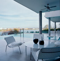 Blick vom Balkon mit weißem Gartentisch und Stühlen auf die Pool-See-Terrassen und den modernen Außenbereich