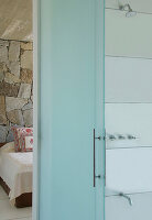 View through glass door of en suite bathroom to bedroom with exposed stone wall