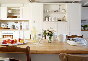 Pfirsiche und Geschirr mit geschnittenen Rosen auf Holztisch in Landhausküche