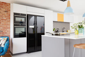 Moderne mehrfarbige Einbauküche mit schwarzen Geräten und geometrischer Spritzschutzwand London UK