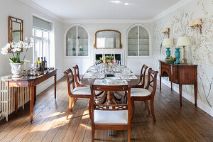 Oval dining table with chairs and antique consoles in dining room