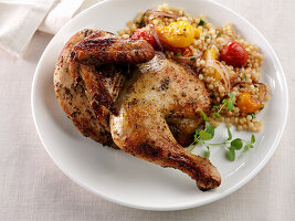 Half of an oven roast chicken with couscous and cherry tomatoes
