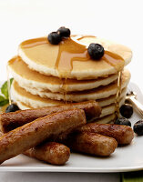 A stack of buttermilk pancakes with breakfast sausage links, blueberries and maple syrup