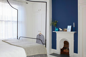 Queen bed with canopy, white floor-to-ceiling built in wardrobe and fireplace against blue wall in bedroom