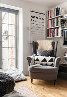 Light grey wing chair with cushions, bookshelf and wall map