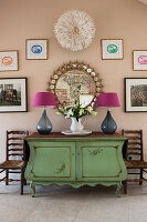 Antique Swedish chest with table lamps below photographs, mirror and juju hat on wall