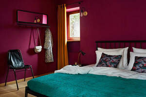 Schlafzimmer mit Wänden in Magenta, petrolfarbener Decke und schwarzem Metallbettgestell