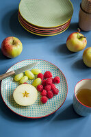 Apfel, Weintrauben und Himbeeren mit Messer auf Keramikteller