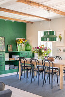 Dining area with green wall and green chest of drawers, wooden table and black chairs