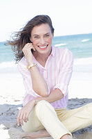 Brunette woman in pink striped blouse and light shorts on the beach