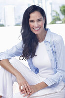 Dark-haired woman in a white top, light blue shirt and white trousers