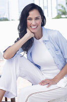 Dark-haired woman in a white top, light blue shirt and white trousers