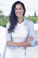 Dark-haired woman in a white top, light blue shirt and white trousers