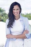 Dark-haired woman in a white top, light blue shirt and white trousers