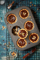 Freshly decorated chocolate caramel tarts in a baking tin with sea salt and sprinkles
