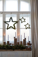 Hanging stars made of moss, candles and fir branches as Christmas window decorations